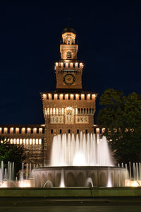 Low angle view of illuminated fountain against buildings at night