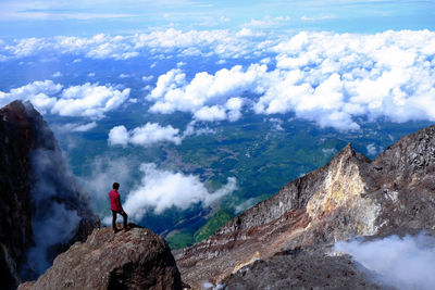 High angle view of male hiker standing on mountain against clouds