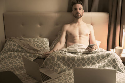 Portrait of mature man using mobile phone while sitting on bed