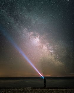 Person lighting sky with flashlight against star field at night