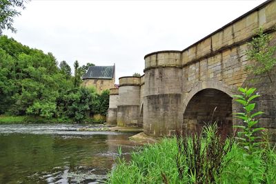 Arch bridge over river by buildings against sky