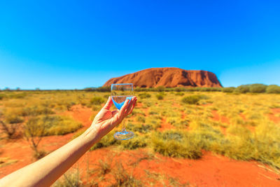 Person holding umbrella on landscape against clear blue sky