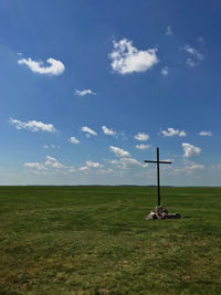 Scenic view of field and cross against sky