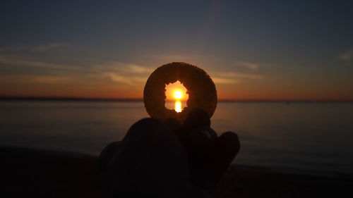 Close-up of hand holding sun during sunset