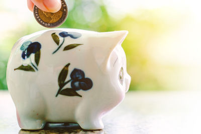 Cropped hand inserting coin in piggy bank on table