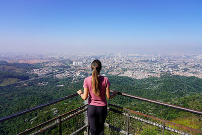 Rear view of woman standing on railing against clear sky