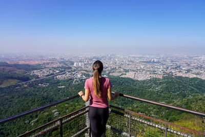 Rear view of woman standing on railing against clear sky