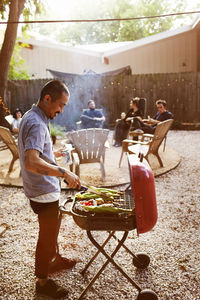Man barbecuing while friends sitting in yard