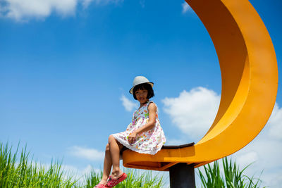 Low angle view of girl sitting on land against sky