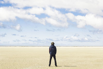 Rear view of woman standing on beach against sky