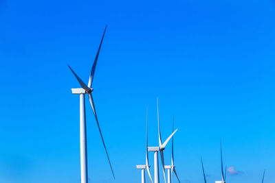 Low angle view of windmills against clear blue sky