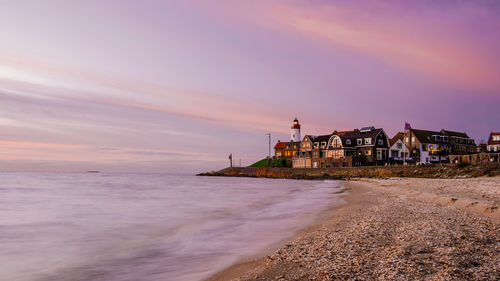 Sea and buildings against sky during sunset