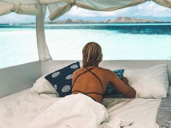 Rear view of woman relaxing on bed at beach