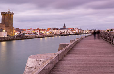 Bridge over river by buildings in city against sky