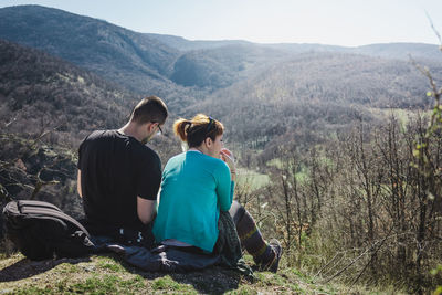Couple sitting on mountain against clear sky