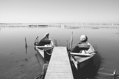 Boats moored at pier on lake against clear sky