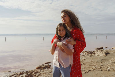 Young woman standing at beach hugging daughter