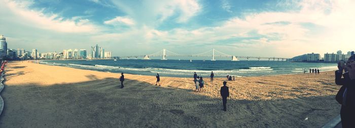 Panoramic view of people at beach with gwangandaegyo over sea against sky