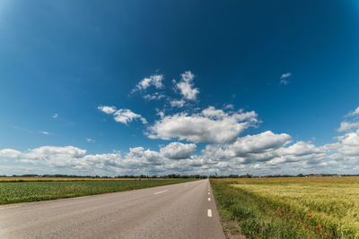 Street amidst grassy field against sky