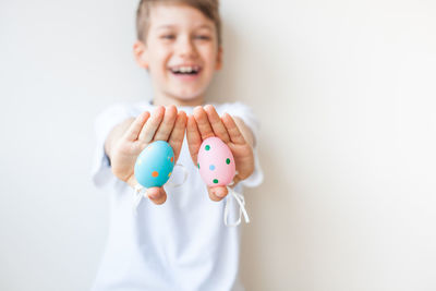 Cheerful boy holding easter eggs while standing against wall