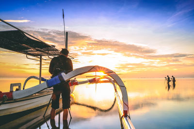 Men standing by boat in sea against sky during sunset