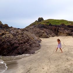 Side view of girl playin on deserted  beach against sky