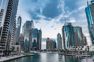 Modern buildings by river against sky in city