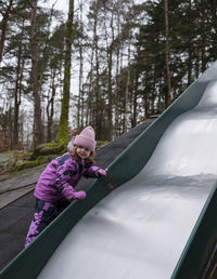 Girl in pink winter clothes climbing up slide