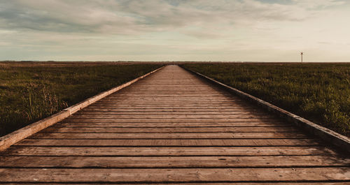 View of wooden boardwalk on field against sky