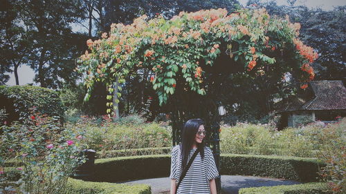 Woman standing by flowering plants against trees