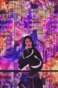 Portrait of young woman standing against illuminated wall