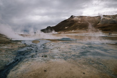 Steam emitting from geyser against cloudy sky