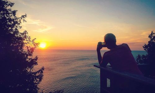 Man looking at sea against sky during sunset