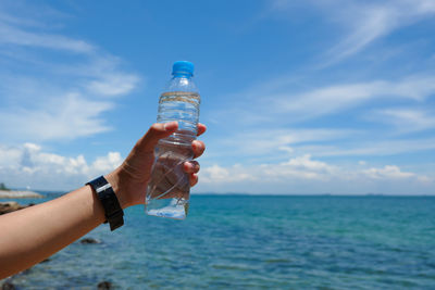 Hand holding bottle against sea and sky