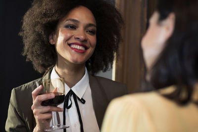 Smiling woman talking to friend while having wine at home