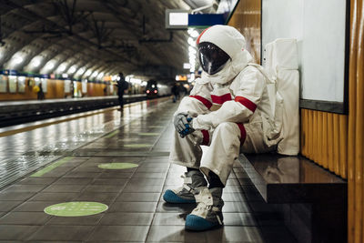 Male astronaut sitting on bench at railway platform