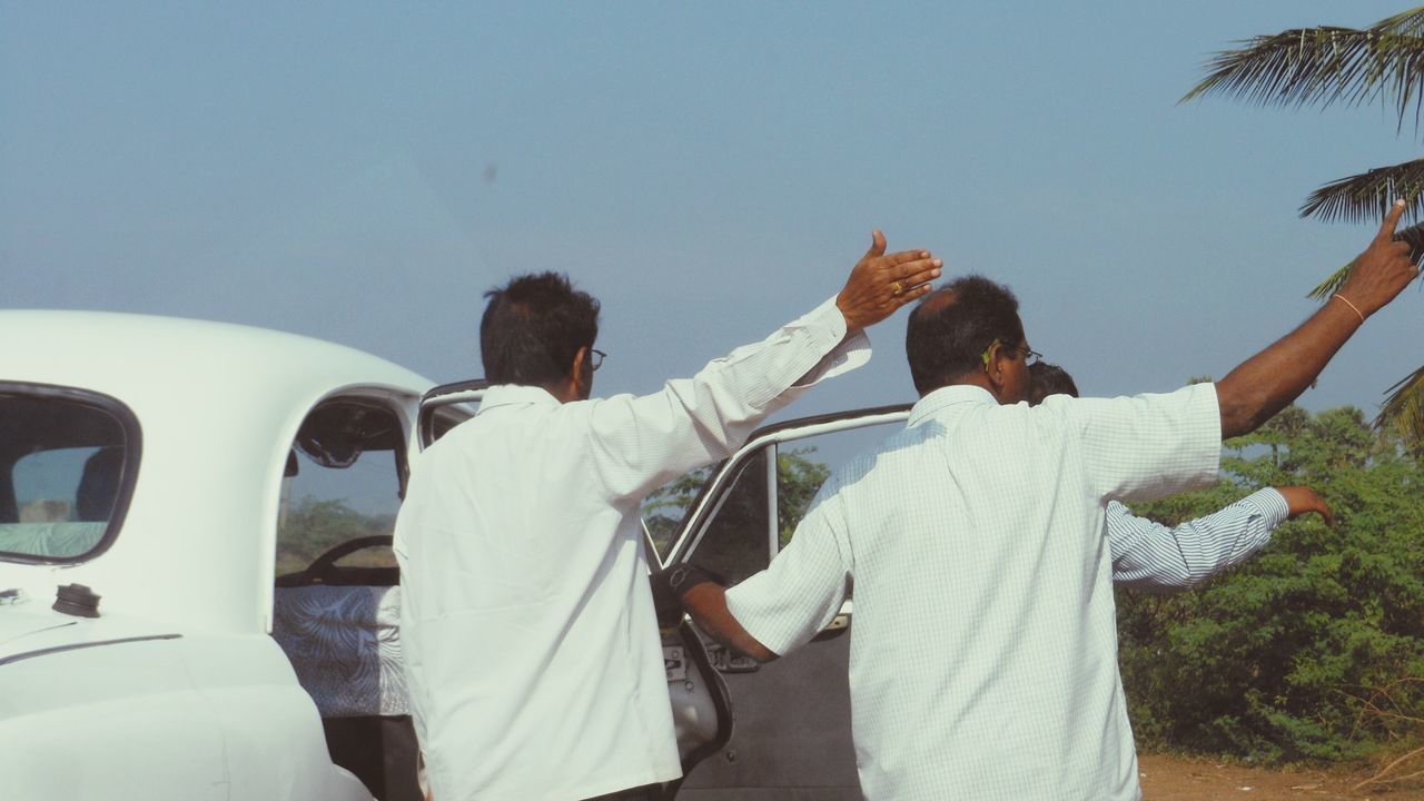 REAR VIEW OF PEOPLE STANDING ON STREET AGAINST SKY