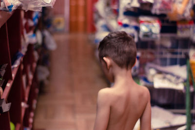 Rear view of shirtless boy by shelves