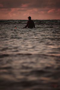 Silhouette person in sea against sky during sunset