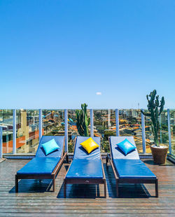 Deck chairs by swimming pool against clear blue sky