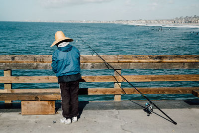 Rear view of man standing by railing against sea