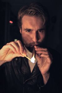 Portrait of young man lighting cigar in darkroom