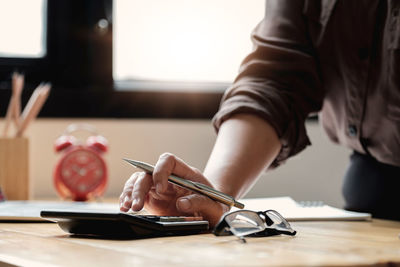 Midsection of businesswoman using calculator on table