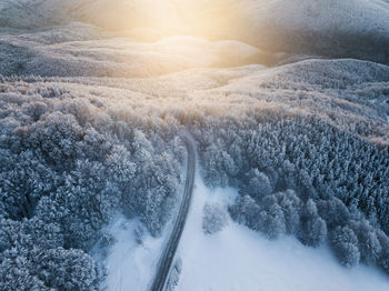 Scenic aerial view of snow covered winter landscape and empty asphalt road at sunrise. 