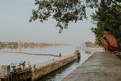 Man sitting by lake against sky