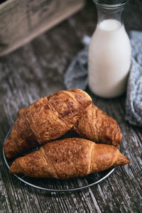 View of freshly baked croissants on wooden table with bottle of milk in the background 