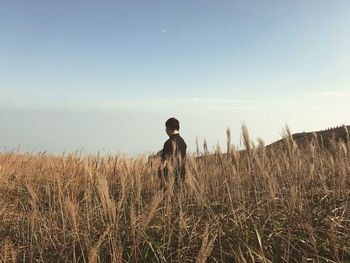 Side view of woman standing at field against sky