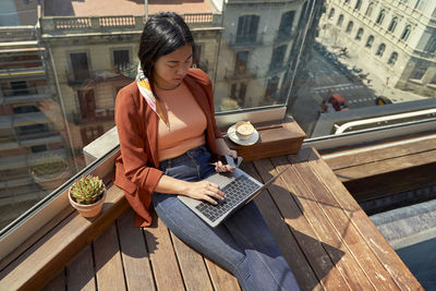 Young woman using laptop while sitting at roof terrace on sunny day