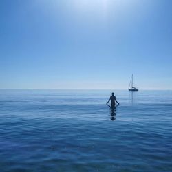 A woman bather swims across a flat calm. sea to her yacht 