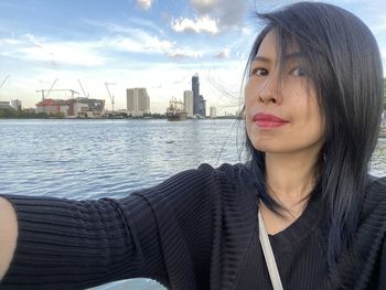 Portrait of beautiful young woman in city against sky